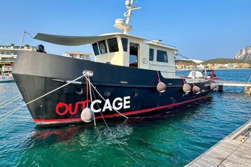 A boat named 'OUTCAGE' docked at a pier with clear blue water and buildings in the background. 1