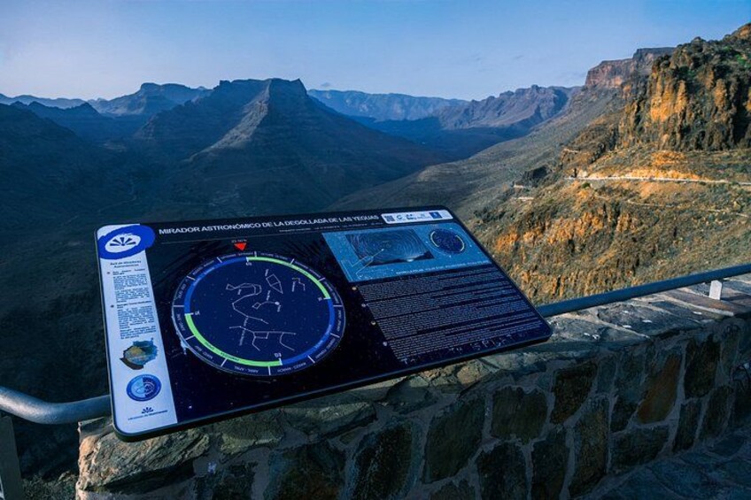A panoramic view of a mountainous landscape with a visitor information board displaying a map and text. 2