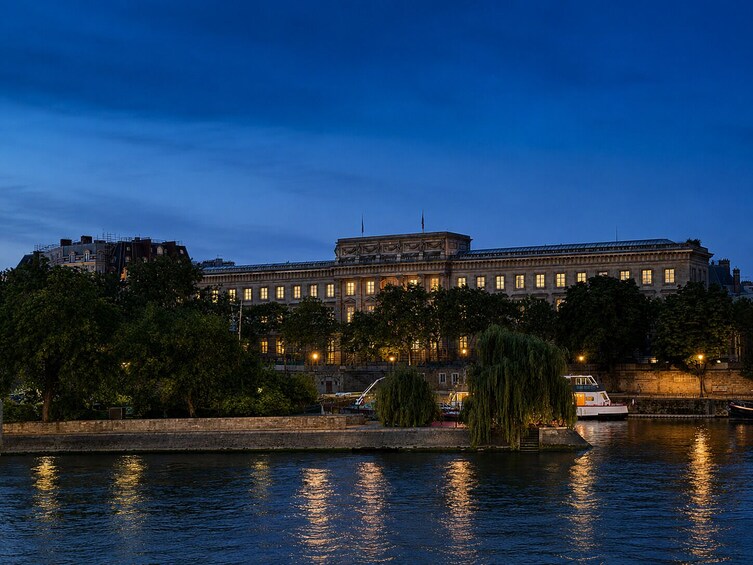 A large, illuminated building by a calm river at dusk. 2