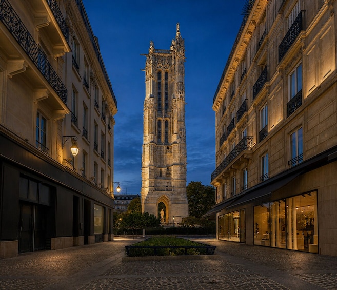 A historic tower with intricate architecture, a cobblestone street, and surrounding buildings with illuminated windows. 5
