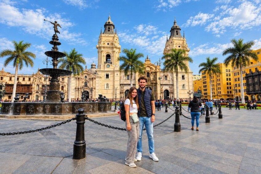 A couple standing in front of a historic building with a fountain and palm trees. 1