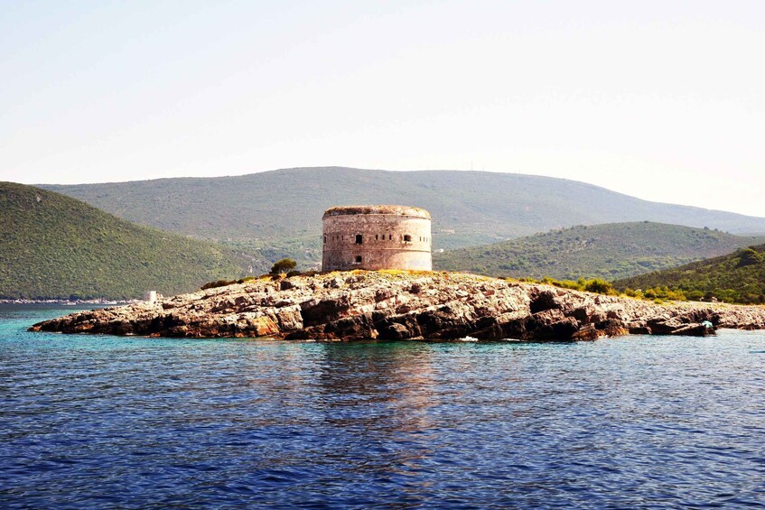 A historic tower on a rocky island surrounded by clear blue waters and green hills. 1