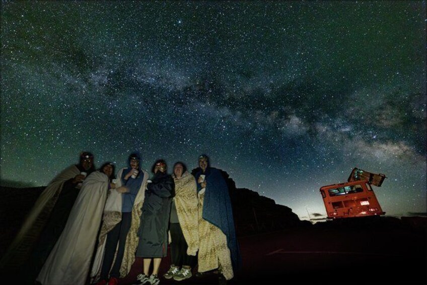 A group of people standing under a starry sky with a bus in the background. 1