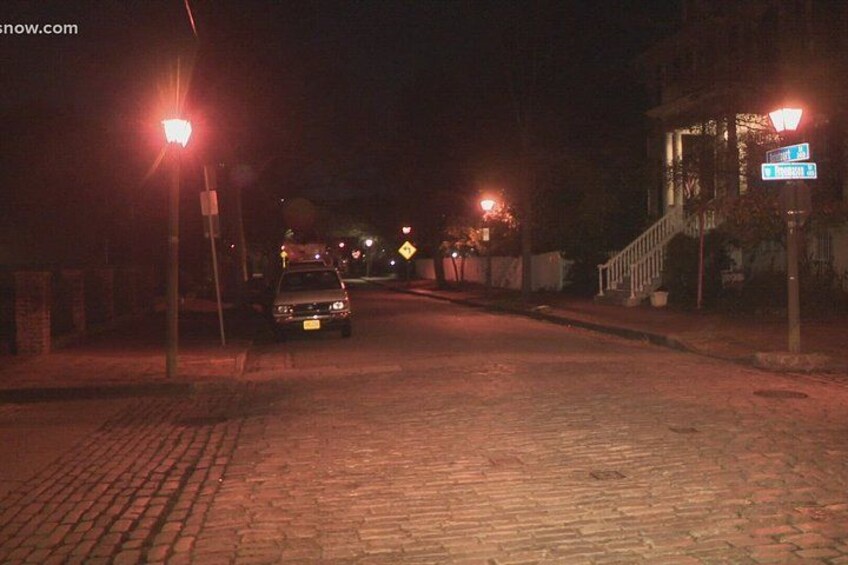 A nighttime street scene with a car parked on the side, street lamps, and a building with a staircase. 2
