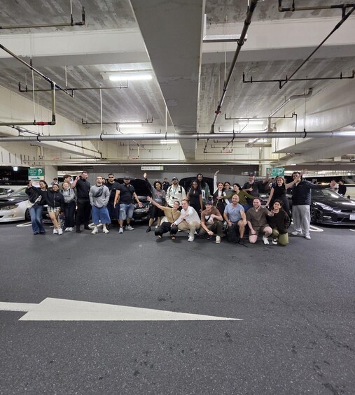 A group of people posing in a parking garage with cars and exit signs. 4