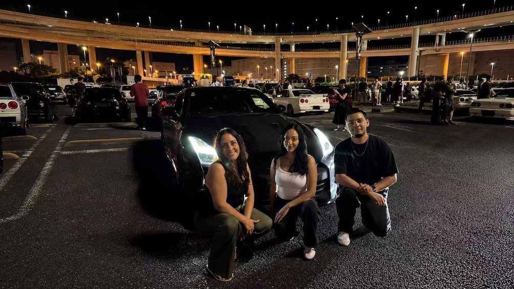 A nighttime parking lot with multiple cars and a large overpass in the background. 5