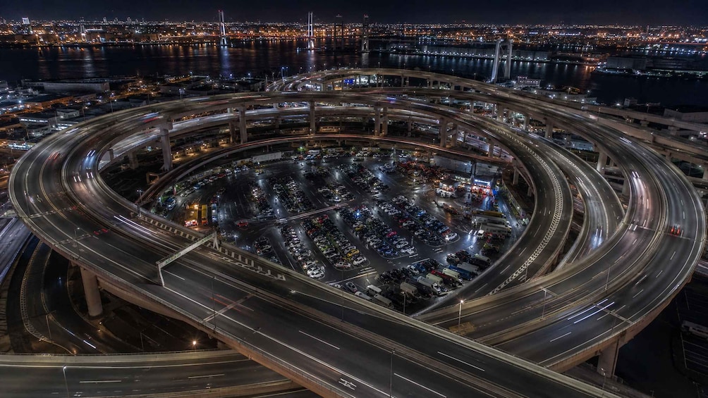 A multi-level highway interchange with vehicles in motion, surrounded by city lights and a body of water. 4
