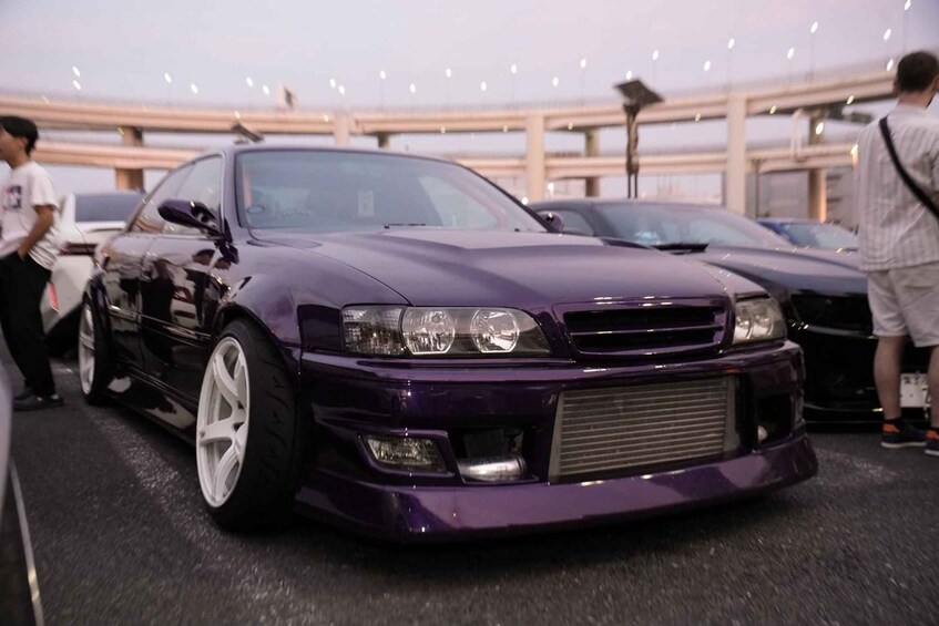 A purple sports car parked in an indoor event space with other vehicles and people in the background. 2