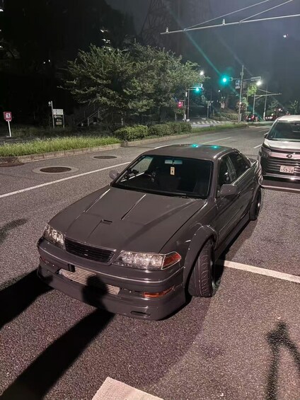 A dark-colored car parked at a street intersection with traffic lights and a pedestrian crossing sign. 5