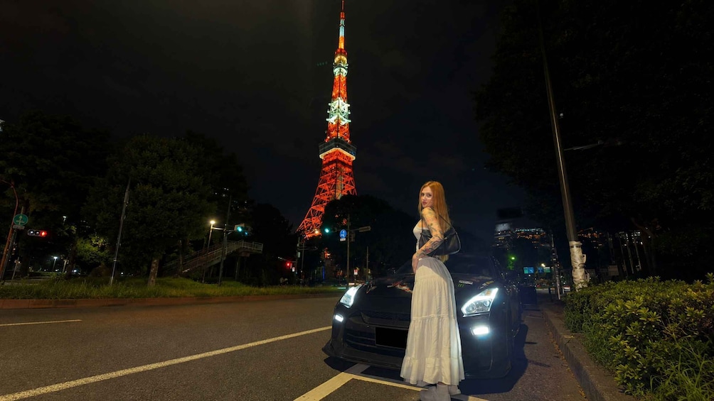 A person standing next to a car with a brightly lit tower in the background. 3