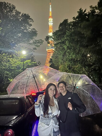 A person holding a transparent umbrella with lights, a car, and a tower with lights in the background. 5