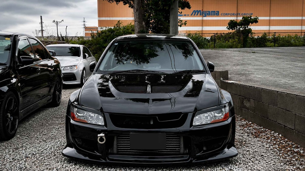 A black sports car parked in front of a building with a sign that reads 'Miyama Corporate Group.' 4