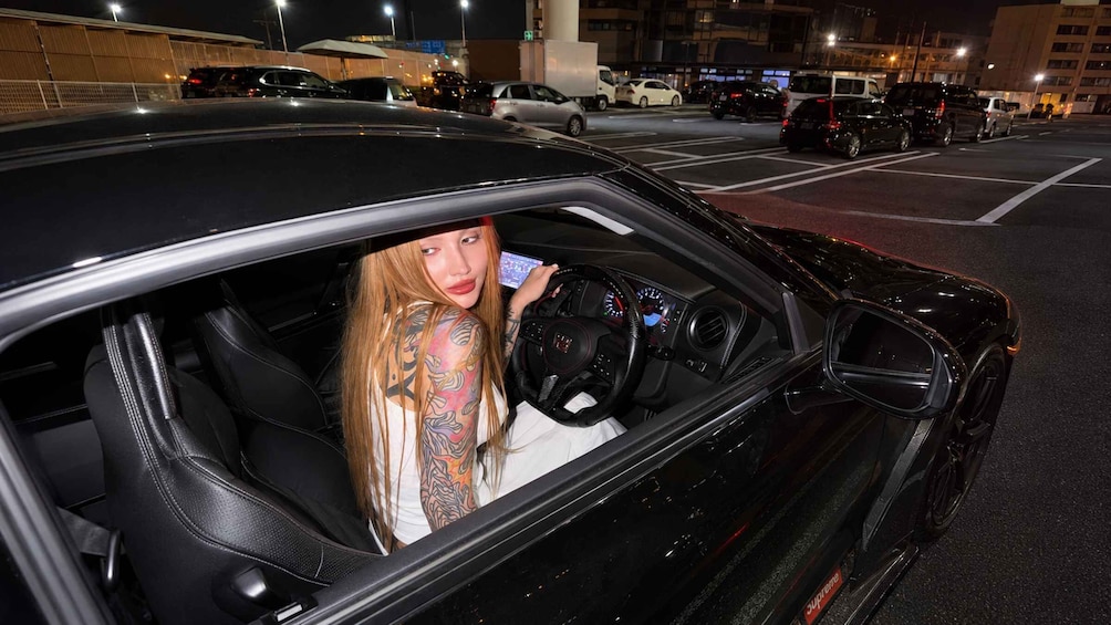 A person with tattoos sitting in a black car at night. 1