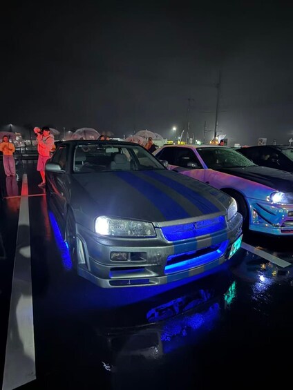 A car with blue underglow lights parked in a lot at night. 2