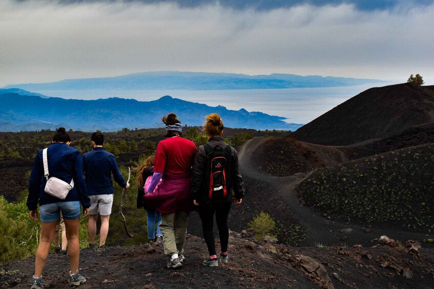 A group of hikers on a rocky trail with a view of distant mountains and a body of water. 1