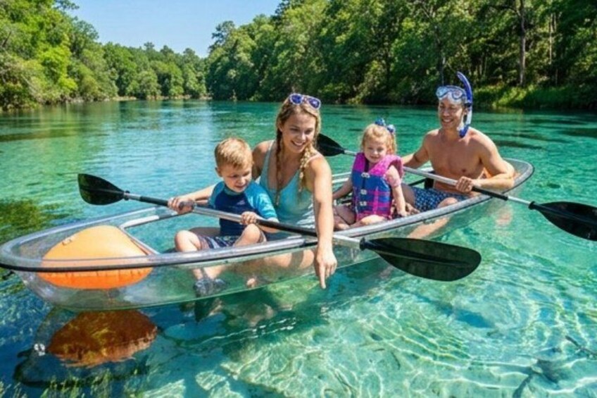 A family in a transparent kayak on a clear river surrounded by greenery. 2