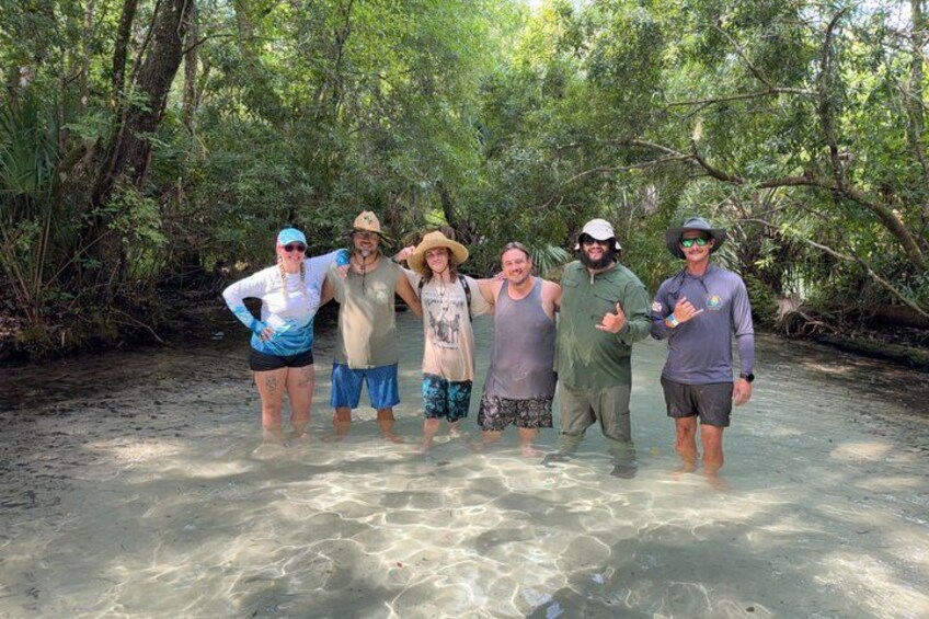 A group of people standing in shallow water surrounded by dense forest. 3