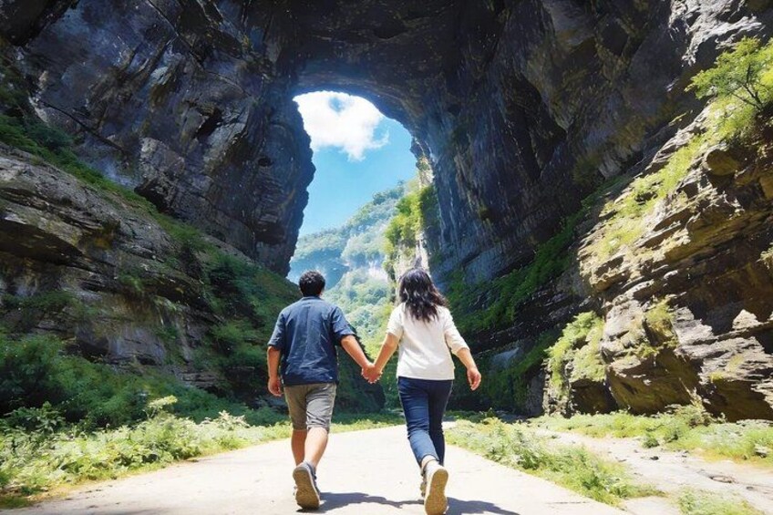 A couple walking on a path through a rock arch formation. 2