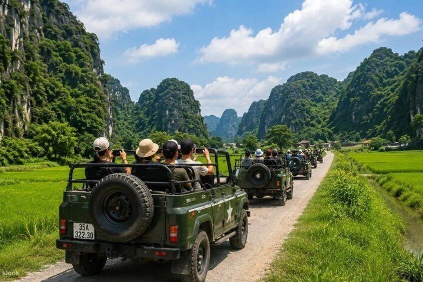 A convoy of jeeps on a rural road with lush greenery and limestone cliffs. 2