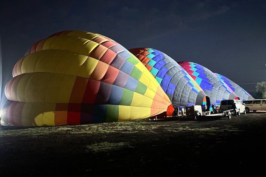 Una fila de coloridas globos aerostáticos estacionados en un campo por la noche. 5