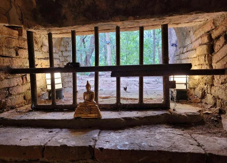 En gyllene Buddha-staty i ett svagt upplyst rum med stenmurar och gallerförsedda fönster. 4