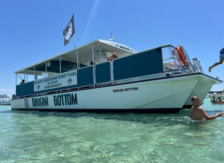 A boat named 'Bikkini Bottom' with a flag, a lifebuoy, and clear water. 1