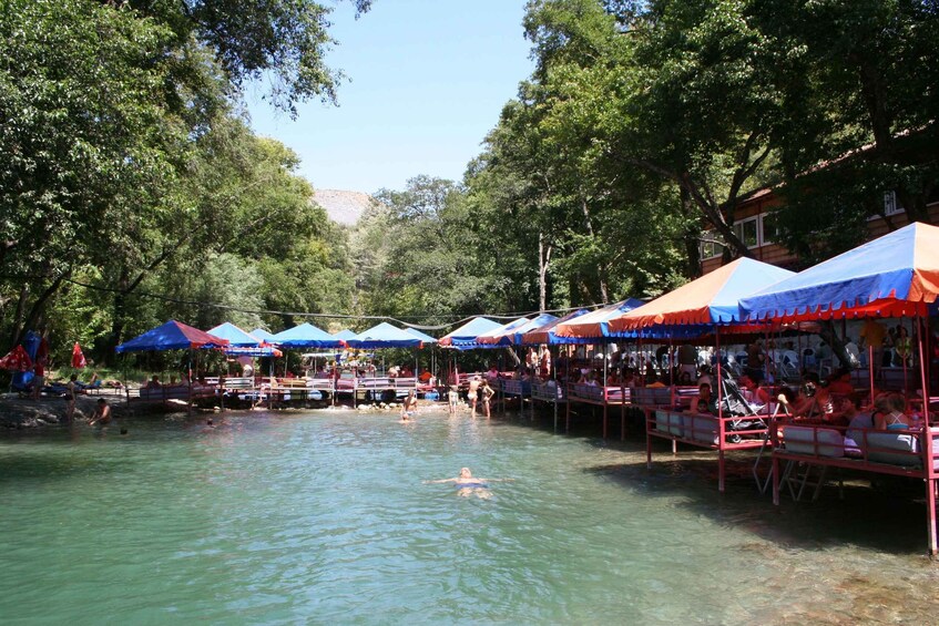 A riverside market with canopies and people swimming. 5