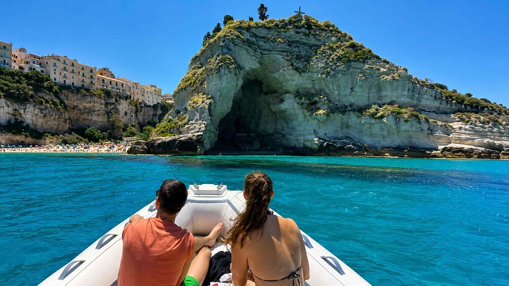 A couple on a boat with a rocky cliff and buildings in the background. 4