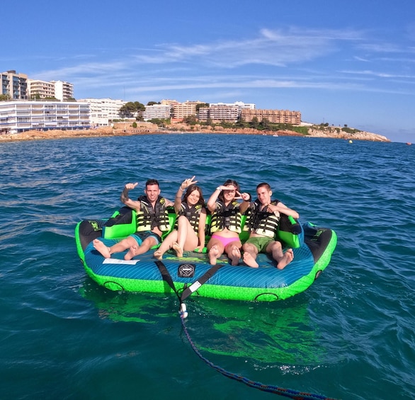 A group of people on a green inflatable raft in the water with buildings in the background. 1