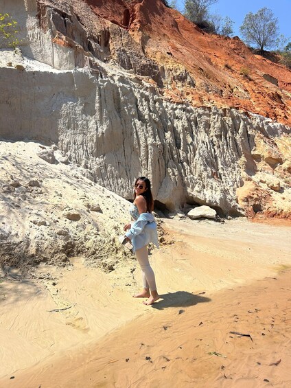 A person standing on a sandy beach with white rock formations and red cliffs in the background. 2