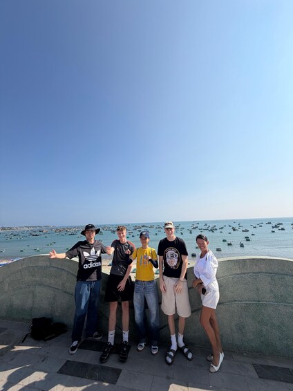 A group of people standing by a waterfront with boats in the background. 4