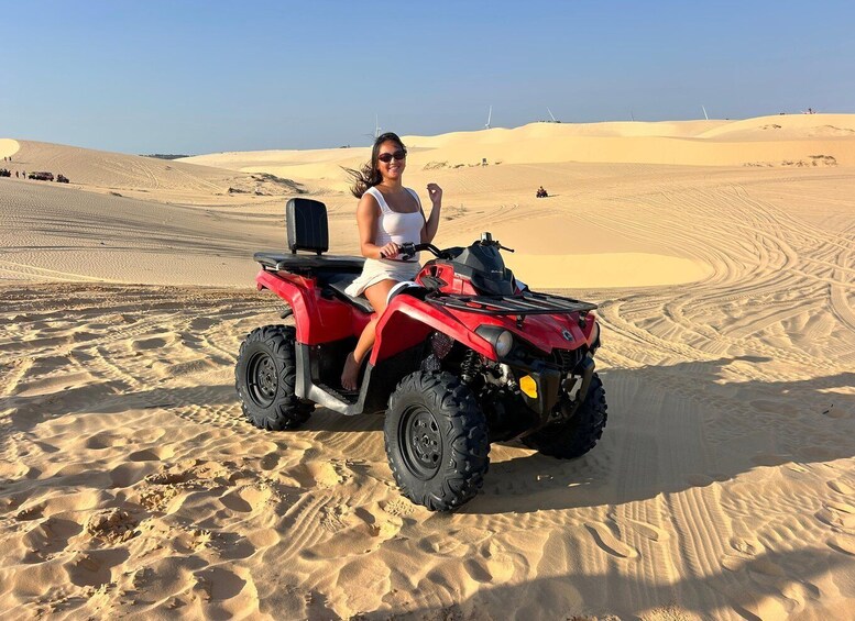 A person on a red quad bike in a desert with sand dunes and wind turbines in the background. 1