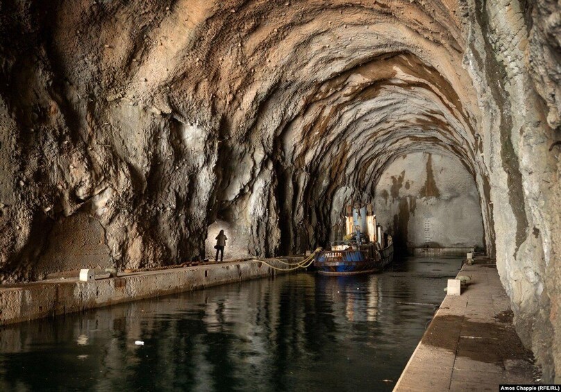 A narrow, rocky tunnel with a boat moored at the end. 3