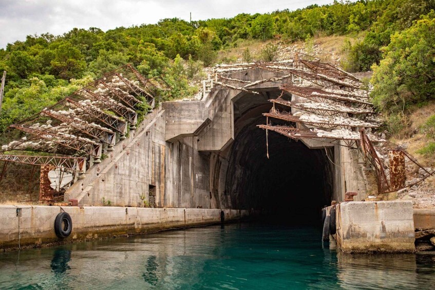 A concrete tunnel with rusted metal structures and vegetation growing over it. 4