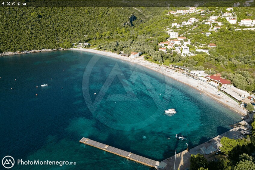 An aerial view of a coastal town with a pier extending into the sea, surrounded by lush greenery and white buildings. 5