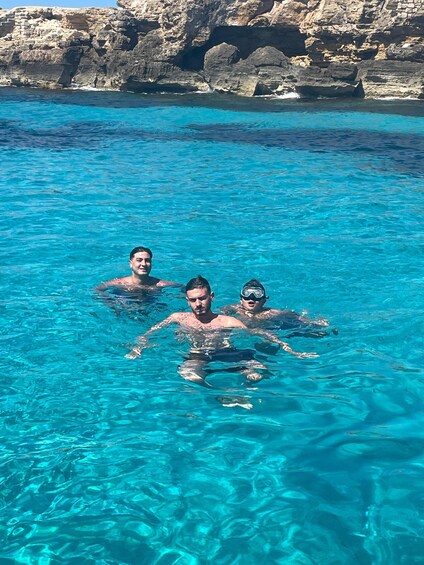 Three people swimming in a clear blue pool with rocky cliffs in the background. 2