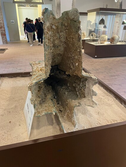 A large, weathered stone structure with a central opening, surrounded by a sandy base, in an indoor exhibit. 5