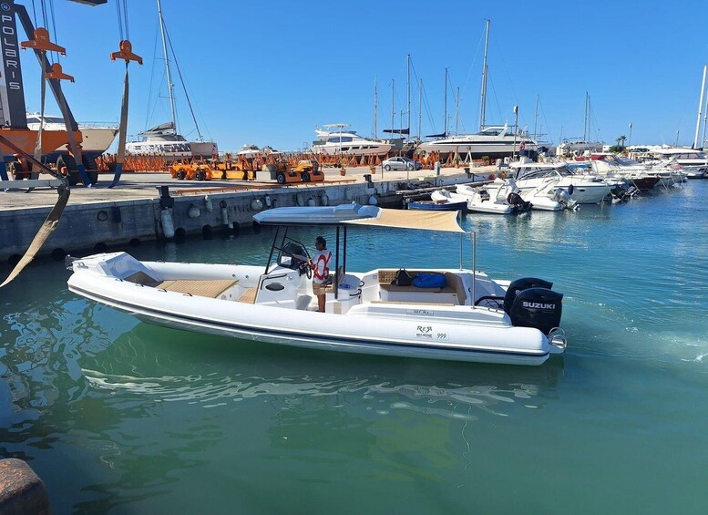 A marina with various boats docked, a person on a small white boat, and a crane in the background. 1