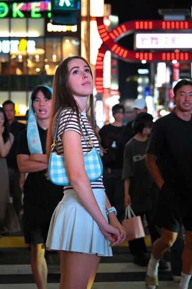 A person standing in a busy urban area with bright lights and signs in the background. 2
