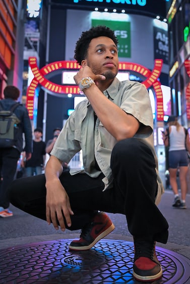 A person crouching on a tiled surface with a city street and illuminated signs in the background. 3