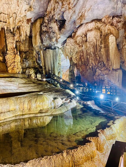 A cave with stalactites and stalagmites, a water pool, and a wooden walkway. 5