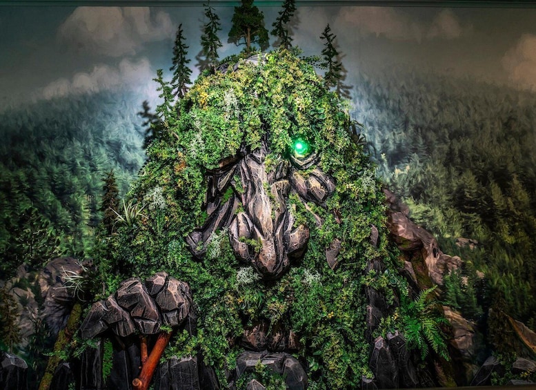 A forested area with a large rock formation covered in greenery and a green light at the top. 2
