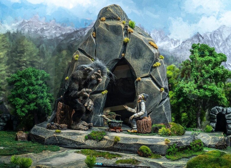 A rock formation with a cave entrance, a seated figure, and a standing figure with a staff. 1