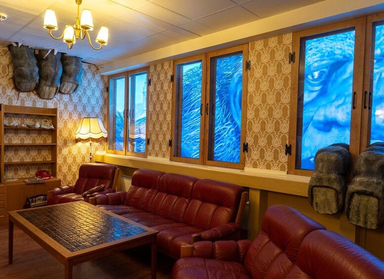 A cozy living room with leather sofas, a patterned wallpaper, and a large window with a blue abstract design. 3