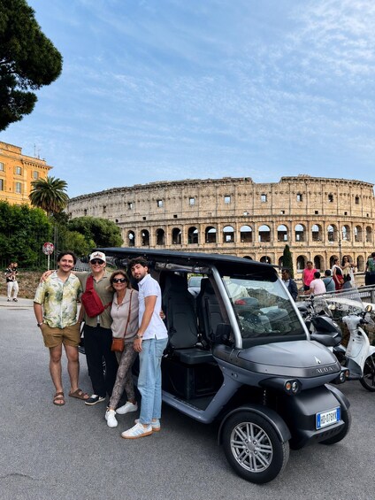 A group of people posing in front of the Colosseum with a black electric vehicle parked nearby. 1