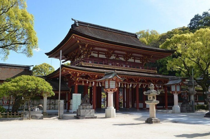 A traditional Japanese temple with a large wooden gate, stone lanterns, and a clear sky. 1