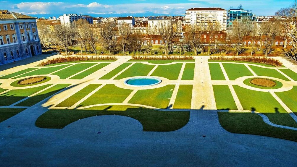 A park with geometric landscaping, a central pond, and surrounding buildings. 4