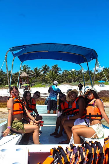 A group of people on a boat with a canopy, wearing life jackets, and a beach with palm trees in the background. 4