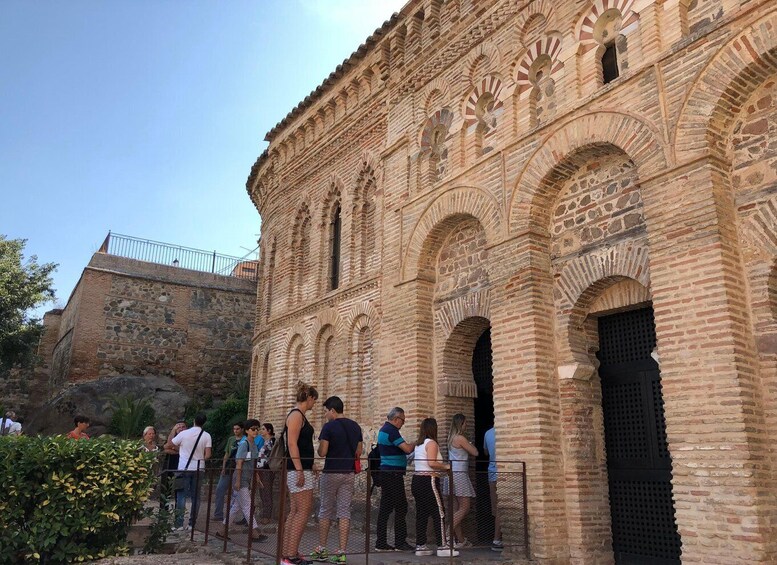 A historic building with arches and intricate brickwork, surrounded by a metal fence and visitors. 5