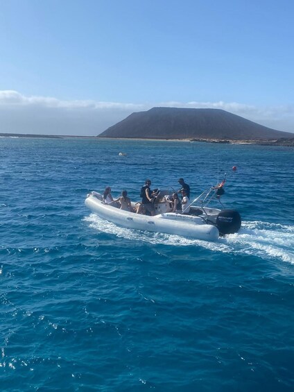 A group of people on a motorized inflatable boat in the ocean with a mountain in the background. 2